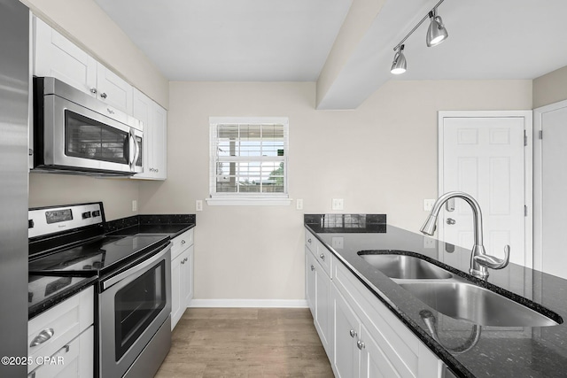 kitchen featuring light wood-style flooring, dark stone counters, appliances with stainless steel finishes, white cabinetry, and a sink