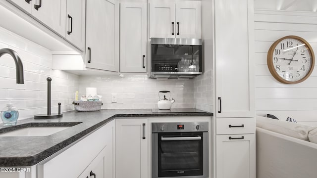 kitchen featuring tasteful backsplash, appliances with stainless steel finishes, dark stone counters, and a sink