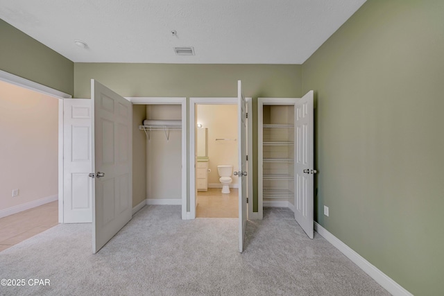 unfurnished bedroom featuring light carpet, visible vents, baseboards, a closet, and ensuite bath