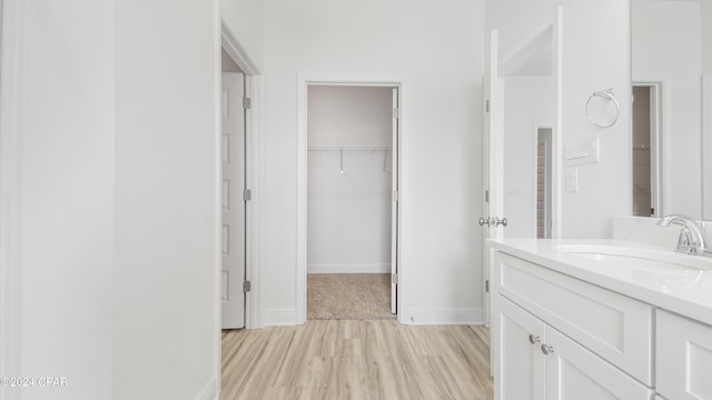 bathroom with baseboards, a walk in closet, wood finished floors, and vanity