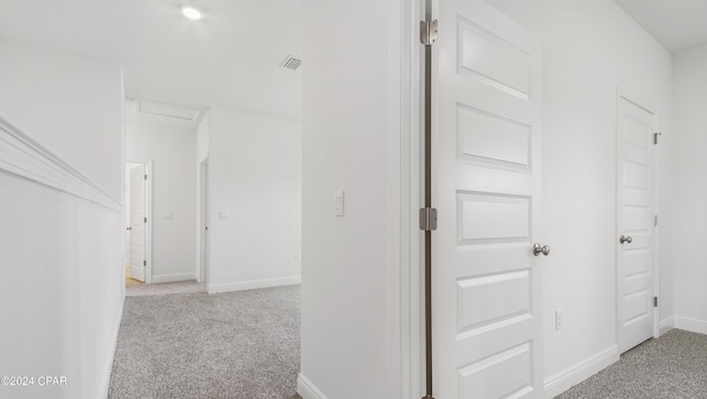 hallway featuring baseboards, visible vents, attic access, and light colored carpet