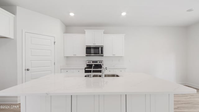 kitchen featuring a kitchen island with sink, baseboards, white cabinetry, a sink, and stainless steel appliances