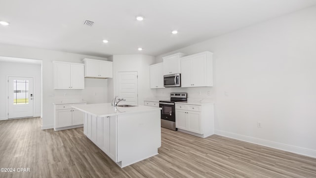 kitchen with a kitchen island with sink, baseboards, appliances with stainless steel finishes, and light wood-style flooring