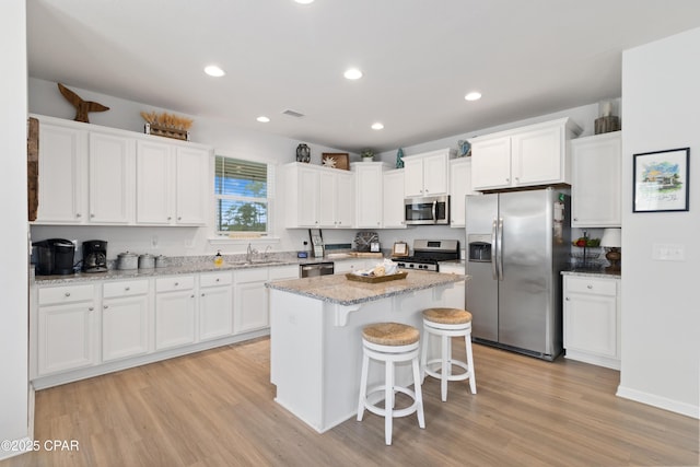 kitchen with white cabinetry, a kitchen bar, light wood-style floors, and stainless steel appliances