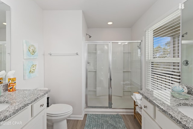 bathroom featuring toilet, two vanities, a shower stall, and wood finished floors