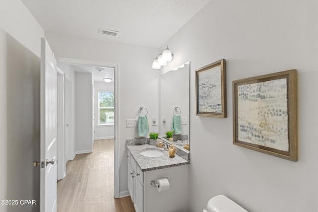 half bathroom with vanity, baseboards, toilet, visible vents, and wood finished floors