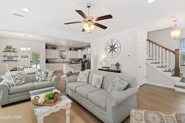 living room with light wood finished floors, visible vents, stairway, and ceiling fan with notable chandelier