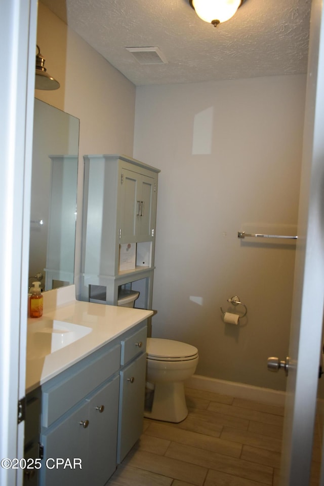 bathroom with wood finished floors, visible vents, toilet, vanity, and a textured ceiling