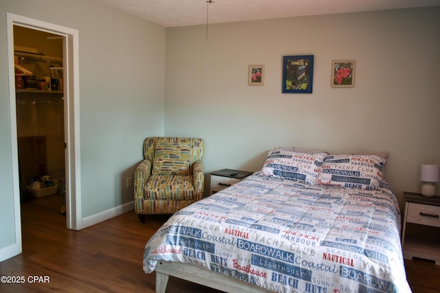 bedroom with a closet, wood finished floors, a spacious closet, and baseboards