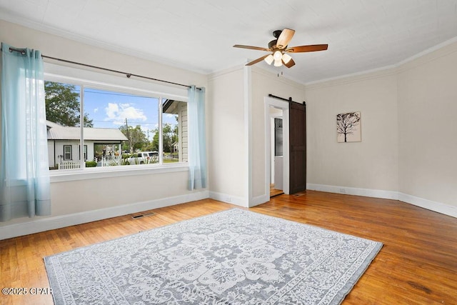 empty room with baseboards, ceiling fan, wood finished floors, ornamental molding, and a barn door