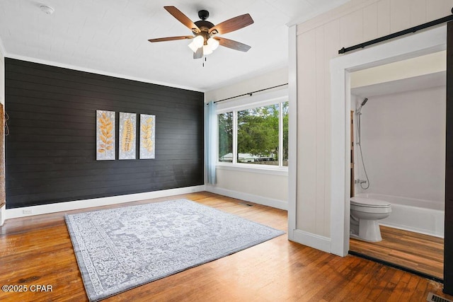 interior space with baseboards, a barn door, wood finished floors, and wooden walls
