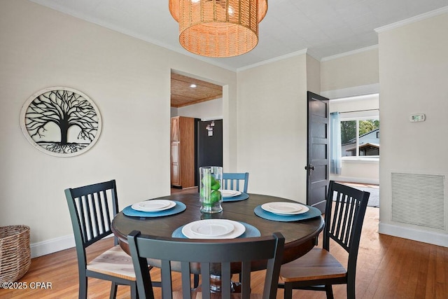 dining area with baseboards, visible vents, wood finished floors, and crown molding