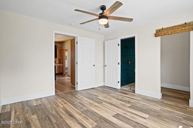 unfurnished bedroom with baseboards, ensuite bathroom, wood finished floors, and a ceiling fan