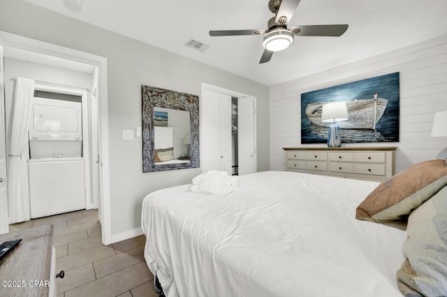 bedroom featuring light tile patterned flooring, baseboards, stacked washer / dryer, visible vents, and a closet