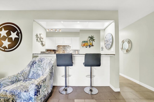 kitchen featuring decorative backsplash, baseboards, a breakfast bar area, tile patterned floors, and white cabinets