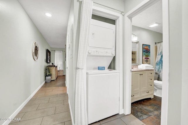 laundry area with baseboards, tile patterned flooring, stacked washer and clothes dryer, and laundry area