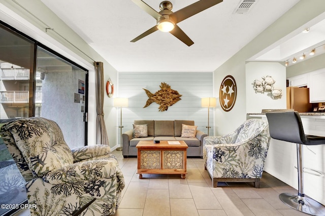 living area featuring light tile patterned floors, ceiling fan, wooden walls, and visible vents