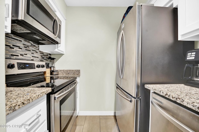 kitchen featuring baseboards, white cabinets, tasteful backsplash, light stone counters, and appliances with stainless steel finishes