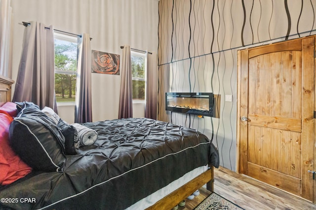 bedroom featuring a glass covered fireplace, a wall mounted AC, and wood finished floors