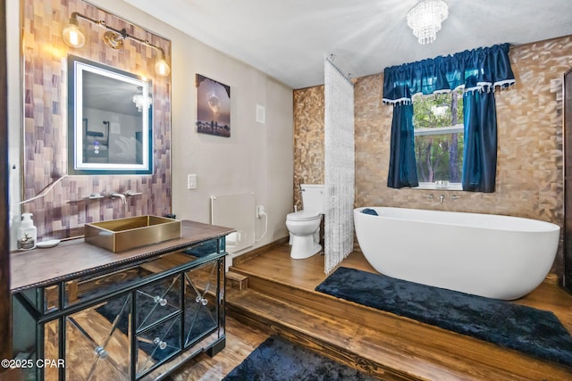 full bath featuring toilet, a freestanding bath, wood finished floors, and vanity