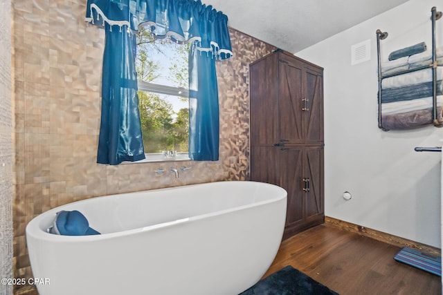 bathroom featuring baseboards, a freestanding tub, wood finished floors, and visible vents
