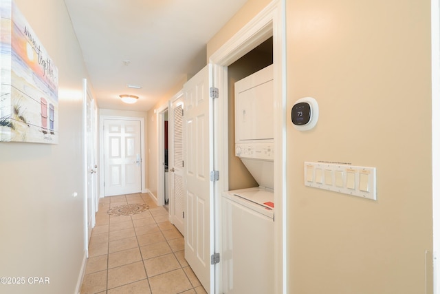 laundry room featuring baseboards, laundry area, light tile patterned flooring, and stacked washer and clothes dryer