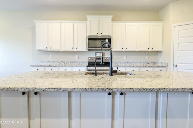 kitchen with stainless steel microwave, white cabinetry, a sink, and an island with sink