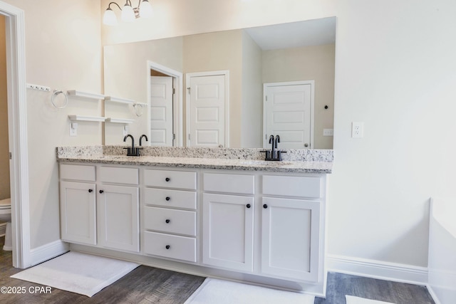 bathroom with double vanity, toilet, wood finished floors, a sink, and baseboards
