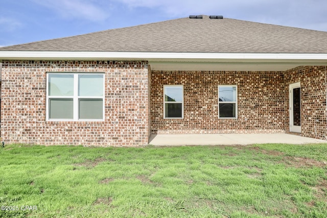 back of house with brick siding, roof with shingles, and a lawn