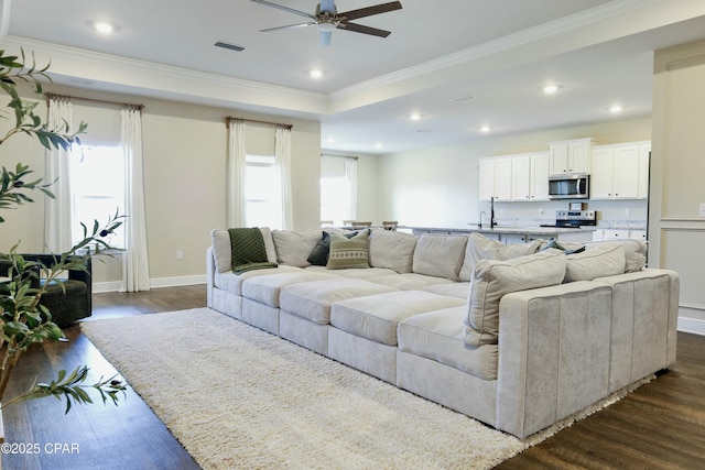 living room with a ceiling fan, a wealth of natural light, visible vents, and dark wood-style floors