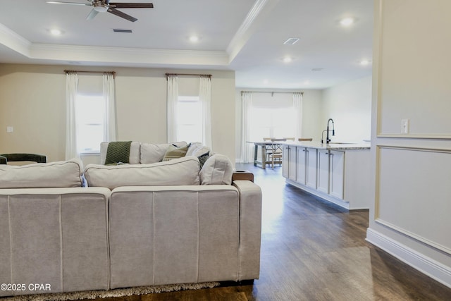 living room with a tray ceiling, ceiling fan, ornamental molding, and dark wood-type flooring