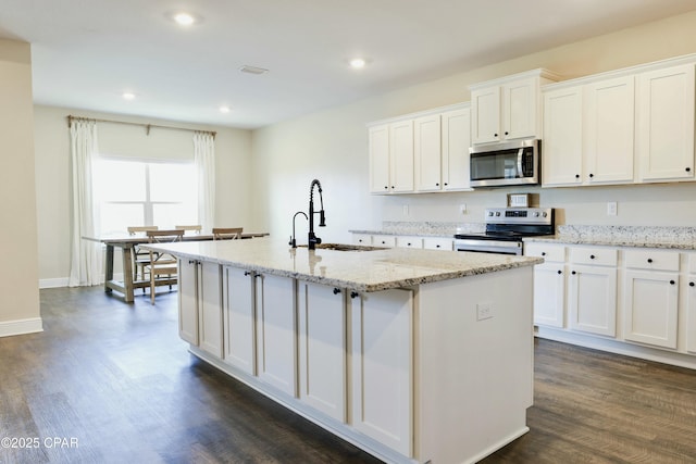 kitchen with a sink, stainless steel appliances, a kitchen island with sink, and dark wood-style floors