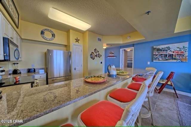kitchen with visible vents, range with electric stovetop, freestanding refrigerator, white cabinetry, and stone counters