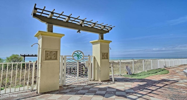 view of patio with a water view, a beach view, fence, and a pergola