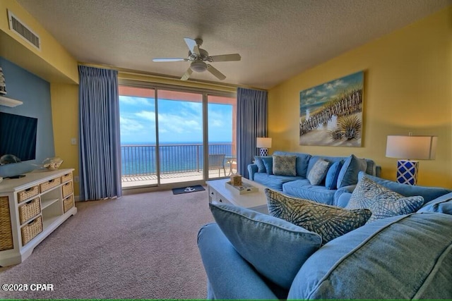 carpeted living room with a textured ceiling, ceiling fan, visible vents, and a water view