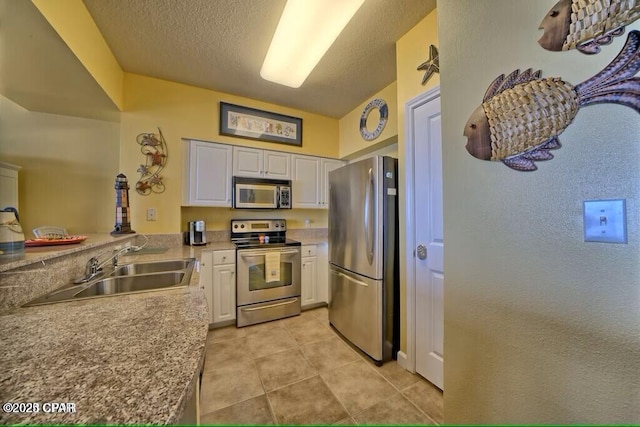 kitchen with light tile patterned floors, white cabinets, a sink, appliances with stainless steel finishes, and a textured ceiling