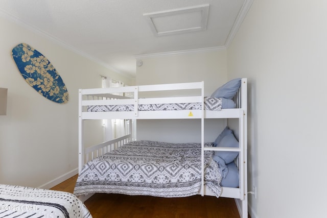 bedroom featuring baseboards, ornamental molding, attic access, and wood finished floors