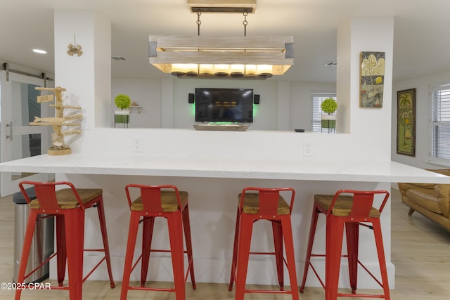 kitchen featuring a barn door, a peninsula, wood finished floors, and a breakfast bar area