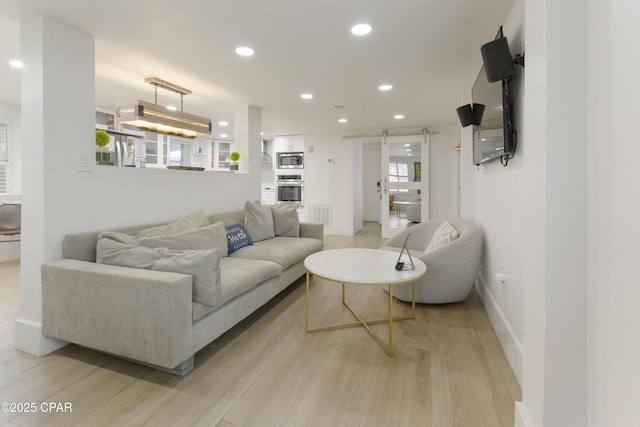 living room with recessed lighting, baseboards, light wood finished floors, and a barn door