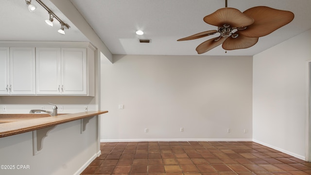 interior space with a kitchen bar, visible vents, ceiling fan, and white cabinets