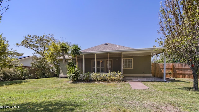 rear view of property with stucco siding, fence, and a lawn