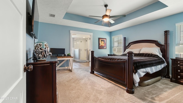 bedroom featuring carpet flooring, a raised ceiling, ensuite bath, and a ceiling fan