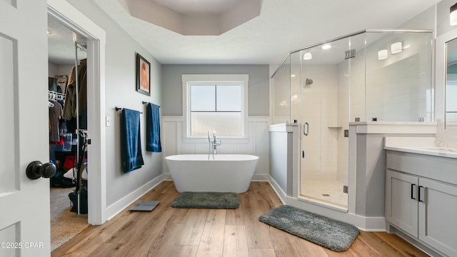 bathroom featuring wood finished floors, a shower stall, vanity, a freestanding tub, and wainscoting