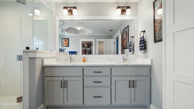 bathroom with a shower stall, double vanity, a sink, and a walk in closet
