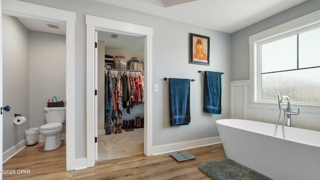 bathroom featuring wood finished floors, a freestanding bath, toilet, a spacious closet, and baseboards