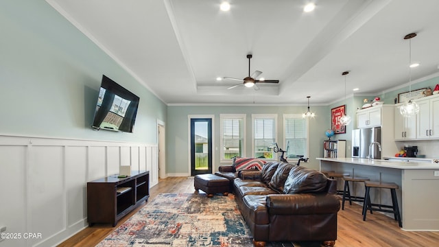 living room featuring a tray ceiling, crown molding, ceiling fan with notable chandelier, and light wood finished floors