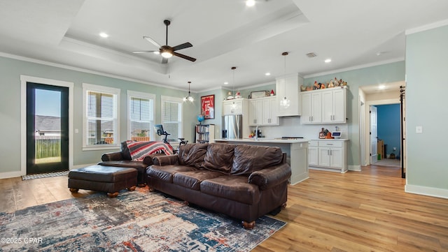 living room with light wood finished floors, ceiling fan, ornamental molding, and a raised ceiling