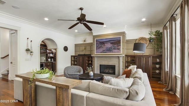 living area featuring stairway, ceiling fan, dark wood-style floors, arched walkways, and a glass covered fireplace