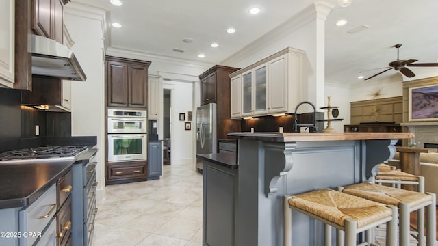 kitchen with crown molding, dark countertops, a breakfast bar, stainless steel appliances, and under cabinet range hood