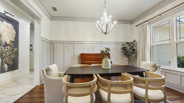 dining area with visible vents, ornamental molding, an inviting chandelier, and a decorative wall